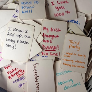 May include: A pile of white cards with handwritten messages in different colours. Some cards say "Someone you used to know well," "I know I love you 1000%," and "Investigating."