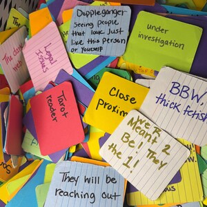 May include: A collection of colorful index cards with handwritten text. Cards are various colors, including pink, yellow, blue, and purple. Text includes phrases like "Tarot reader," "Doppleganger," and "They will be reaching out."