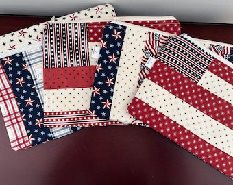 May include: A collection of four rectangular fabric zipper pouches featuring various patriotic patterns in red, white, and blue. The designs include stars, stripes, and plaid motifs. Each pouch has a white zipper closure and a small white brand label.