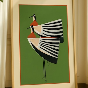 Peut inclure: Impression d'art encadrée représentant deux oiseaux stylisés avec des têtes oranges, des becs noirs et des ailes rayées noires et blanches sur fond vert. L'œuvre est encadrée dans un cadre en bois clair avec un bord rouge, pour la décoration intérieure.
