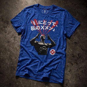 May include: A blue short-sleeve t-shirt featuring a graphic of a muscular figure with red beams emitting from their eyes. The design includes Japanese text and a circular red and white X-Men logo. The shirt has a crew neckline and a size M label.