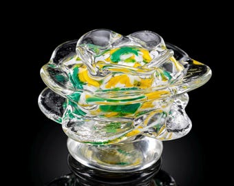 May include: A clear glass sculpture shaped like a flower with ruffled petals. The center of the glass flower features swirling patterns of opaque white, bright yellow, and deep green colors encased within the transparent glass structure.