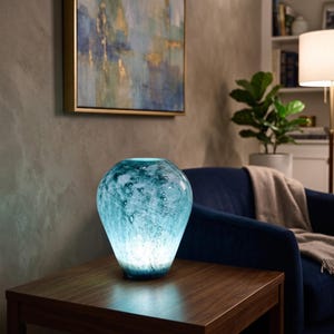 Puede incluir: Una l&aacute;mpara de cristal en forma de l&aacute;grima con un acabado moteado en azul y turquesa. La l&aacute;mpara cuenta con una fuente de luz interna que ilumina el cristal desde dentro, creando un efecto brillante que resalta la superficie y sus matices.