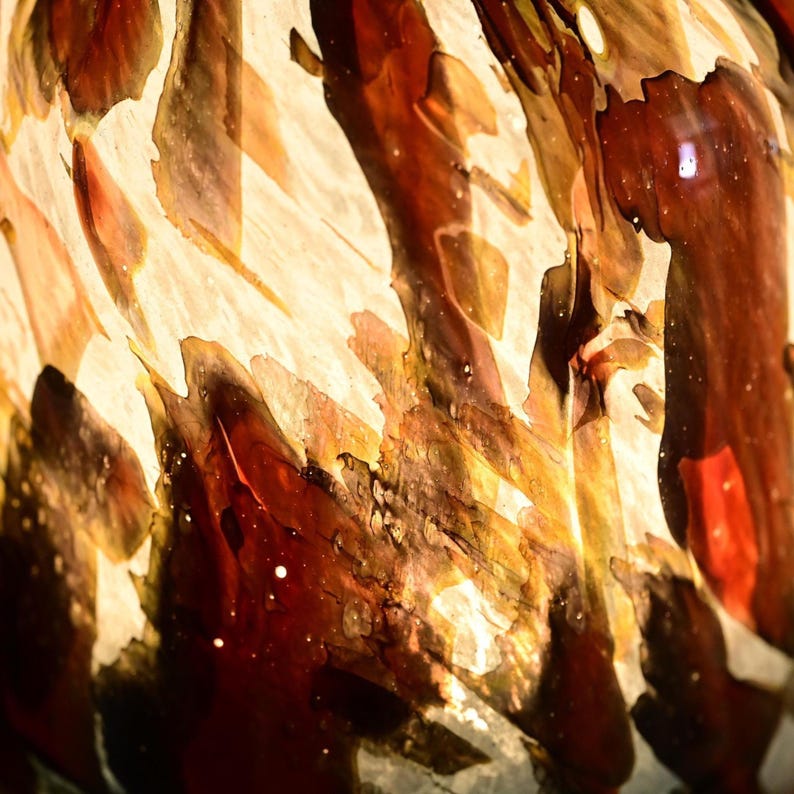 May include: A glass object featuring a swirling, marbled pattern of deep mahogany, amber, and cream colors. The surface displays translucent and opaque layers with organic, irregular shapes that create a complex, layered visual texture throughout.