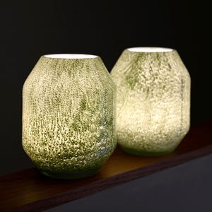 May include: Two cylindrical glass vessels with a textured, mottled surface in shades of light green and white. The glass features a dense, speckled pattern that creates a diffused, glowing effect when illuminated from within, with a wide opening.