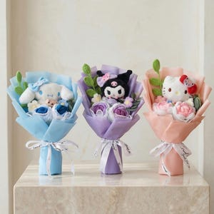 Könnte beinhalten: Drei Plüschtier-Bouquets mit beliebten Charakteren. Jedes Bouquet ist in farbiges Papier gewickelt und mit einem weißen Band gebunden. Die Bouquets umfassen ein blaues, violettes und rosa Farbschema, wobei jedes Bouquet einen anderen Charakter aufweist.