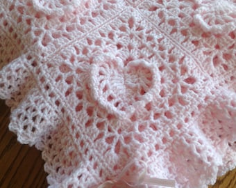 May include: A pink crocheted baby blanket with a delicate lace pattern and a pink satin ribbon tied around it.