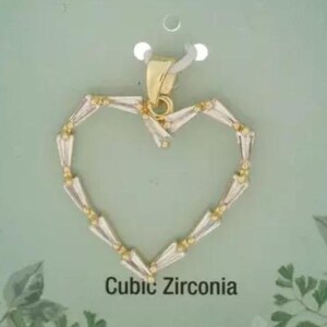 May include: A heart-shaped pendant with a gold-coloured bail and a frame of clear, baguette-cut cubic zirconia stones. The pendant is suspended on a white tag against a light green background. The text "Cubic Zirconia" is printed below the pendant.