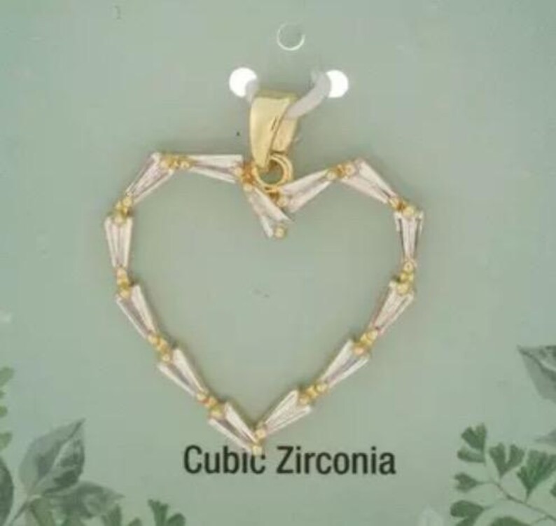 May include: A heart-shaped pendant with a gold-coloured bail and a frame of clear, baguette-cut cubic zirconia stones. The pendant is suspended on a white tag against a light green background. The text "Cubic Zirconia" is printed below the pendant.