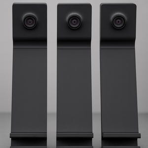 Op de afbeelding: Drie zwarte rechthoekige apparaten met een cirkelvormige lens aan de bovenkant. De apparaten hebben een strak, modern ontwerp met een licht gebogen vorm. De apparaten staan rechtop tegen een grijze achtergrond.