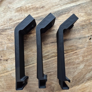 May include: Three identical matte black L-shaped handles with a textured finish. Each handle features a long vertical grip section, a short angled top section, and a hollow rectangular mounting base at the bottom with a circular opening at the top.