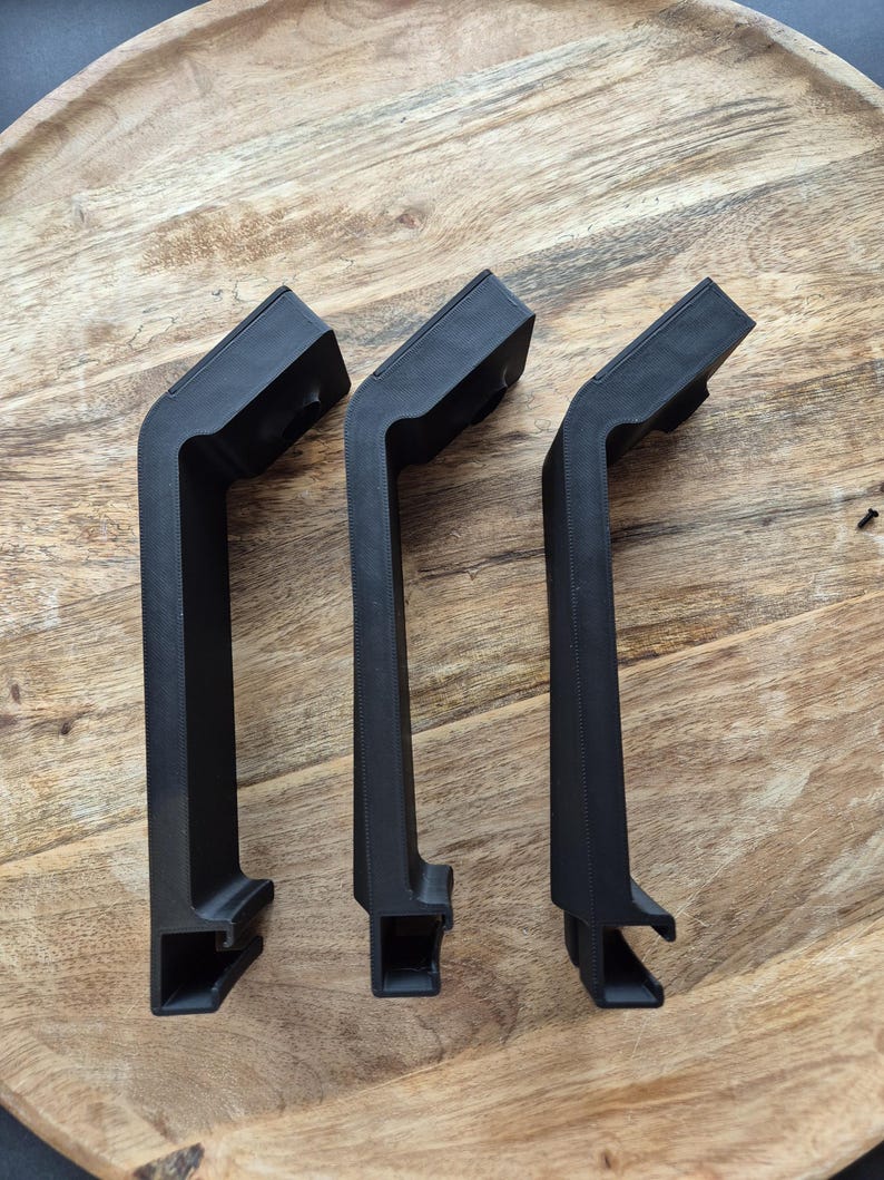 May include: Three identical matte black L-shaped handles with a textured finish. Each handle features a long vertical grip section, a short angled top section, and a hollow rectangular mounting base at the bottom with a circular opening at the top.