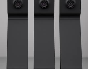 May include: Three matte black vertical stands, each featuring a circular camera lens mounted at the top and a horizontal ledge at the base. The devices have a uniform, elongated rectangular shape with a slight bend near the top section.