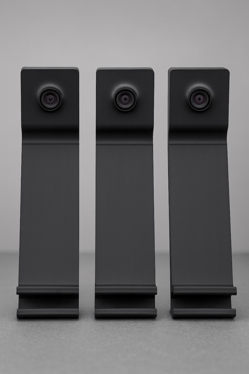 May include: Three matte black vertical stands, each featuring a circular camera lens mounted at the top and a horizontal ledge at the base. The devices have a uniform, elongated rectangular shape with a slight bend near the top section.
