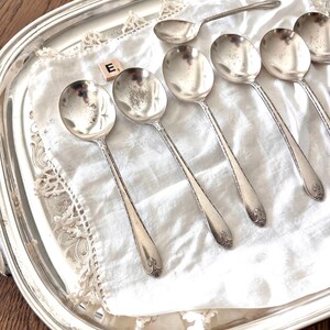 May include: A collection of silver spoons arranged on a silver serving tray with a white cloth. The spoons have ornate handles and rounded bowls. The tray has a decorative edge.