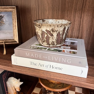 May include: A set of three ceramic mugs with a speckled, matte finish. The mugs are in shades of cream, light gray, and dark gray. Each mug has a simple, minimalist design and a rounded handle.