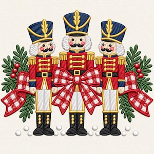 Puede incluir: Un diseño de bordado que muestra tres figuras de cascanueces con uniformes rojos, azules y dorados, con cabello y bigotes blancos. Están dispuestos con ramas de pino verdes, bayas rojas y un gran lazo a cuadros rojo y blanco en el centro.