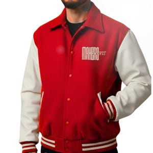 May include: A red and white letterman jacket with the text "MAKERS PIT" in white. The jacket has a red body, white sleeves, and white and red striped cuffs and hem. It features a button-up front and pockets.