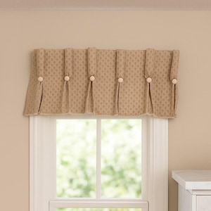 May include: A beige valance with a repeating floral pattern is mounted above a window. The valance is pleated and secured with six wooden buttons. The window is white and has a view of green foliage.