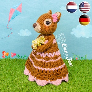 May include: A brown crocheted squirrel wearing a pink dress and holding a bouquet of yellow flowers. The squirrel is standing on a green grassy surface with a blue sky and white clouds in the background.