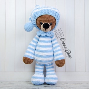 May include: A crocheted stuffed bear wearing a blue and white striped outfit and a matching blue and white striped hat. The bear has brown fur and black eyes.