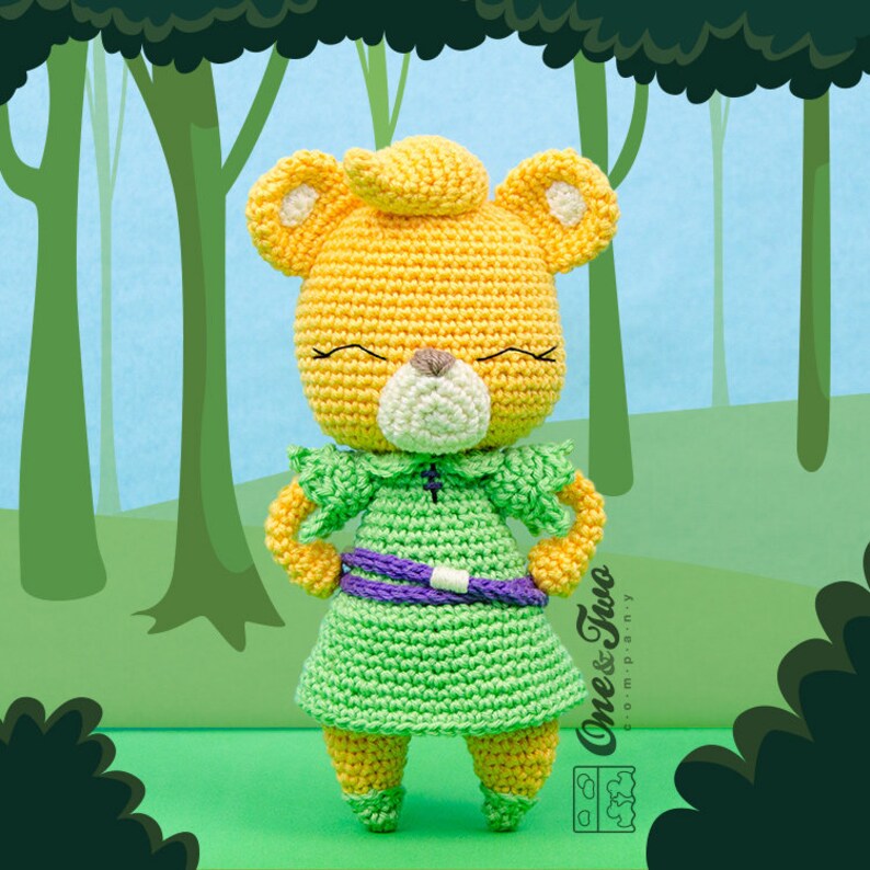 May include: A crocheted plush toy of a yellow bear wearing a green dress with a purple belt. The bear has a white nose and closed eyes. The bear is standing on a green surface with a blue and green background.