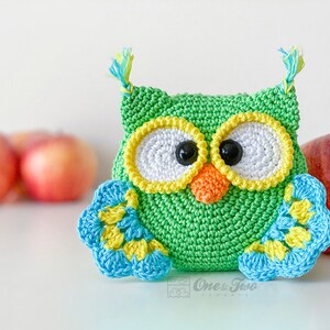 May include: A green crocheted owl with large white eyes, yellow borders, and black pupils. It features an orange beak, blue and yellow wings, and small tufts on top. The text One & Two Company is printed in a small box at the bottom centre.