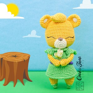 May include: A crocheted yellow bear wearing a green dress and holding a white flower. The bear has closed eyes and a sweet expression. The bear is standing on a green surface with a brown tree stump in the background.