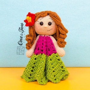 Puede incluir: Una mu&ntilde;eca de crochet con pelo marr&oacute;n, un vestido rosa y verde y una flor roja en la cabeza.