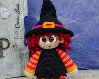 May include: A crocheted witch doll with red hair, a black hat with a pink and orange stripe, and a black and orange striped dress.