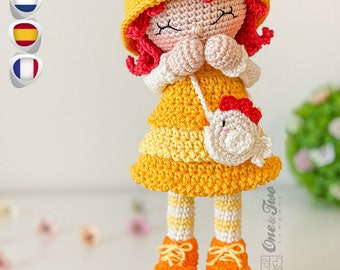 May include: A crocheted doll wearing a yellow and white dress, a yellow hat with a red beak, and orange shoes. The doll is holding a small white crocheted chicken with a red beak. The doll is standing on a cork base with pink and blue flowers.