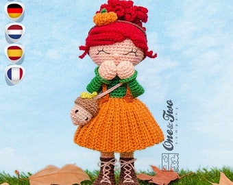 May include: Crocheted doll with red hair, wearing a green and orange dress, holding a small crocheted acorn. The doll is standing on a bed of autumn leaves.