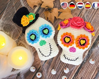 May include: Two crocheted sugar skull ornaments, one with a black top hat and the other with a pink flower crown. Both skulls have colorful flowers and hearts on their faces.