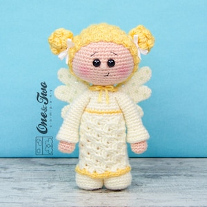 May include: A crocheted angel doll with yellow hair, a white dress, and yellow wings. The doll has a sweet expression and is standing on a wooden surface.
