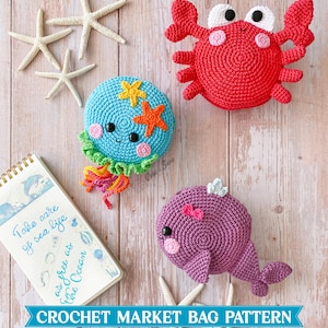 May include: Three crocheted sea creatures including a red crab, a blue jellyfish with orange and yellow starfish, and a purple whale. A spiral-bound notebook features the text "Take care of sea life as free as the Ocean" and the title "CROCHET MARKET BAG PATTERN Sea Life 3-in-1 PDF Bundle".