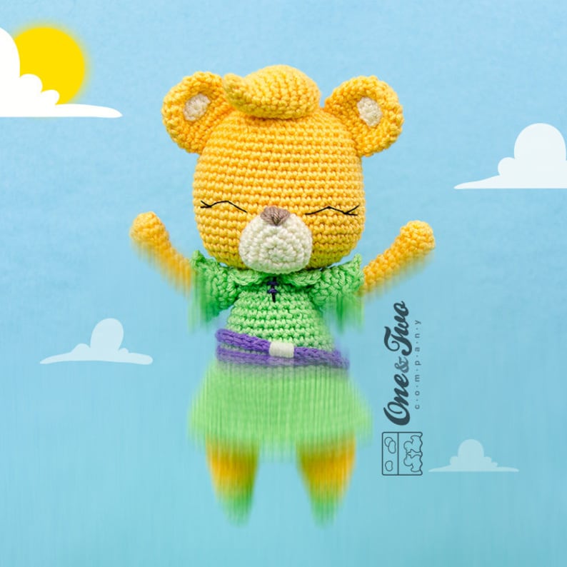 May include: A crocheted yellow bear wearing a green dress with a purple belt. The bear has a white nose and closed eyes. The bear is floating in the air against a blue background with white clouds.