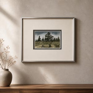 May include: A framed landscape print featuring a forest scene with tall evergreen trees under a cloudy sky. The artwork is set within a silver-toned frame and a cream-colored mat. The print depicts a natural environment.