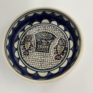 Puede incluir: Un cuenco redondo de cerámica con diseño de mosaico. El cuenco tiene un interior blanco, un borde azul festoneado y un patrón de mosaico en el centro con acentos coloridos. El borde es de color crema claro.