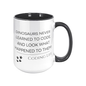 Könnte beinhalten: Weißer Keramikbecher mit schwarzem Innenraum und Henkel. Der Becher zeigt den Text "DINOSAURS NEVER LEARNED TO CODE, AND LOOK WHAT HAPPENED TO THEM! CODING LIFE" in schwarzer Schrift, mit Dinosaurier-Fußabdrücken.