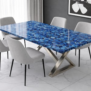 May include: A rectangular dining table with a blue agate stone top and a stainless steel base. The table is surrounded by six gray upholstered chairs with black legs. The room has a modern design with white marble flooring.