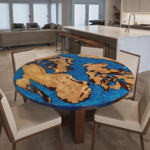 Peut inclure: Une table ronde en bois avec un motif en résine époxy bleue représentant une carte. La table présente un motif de grain de bois naturel et repose sur un socle en bois brun foncé. Elle est entourée de quatre chaises avec des assises crème et des cadres en bois.