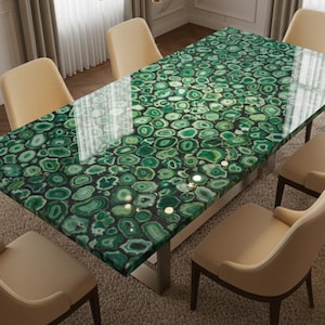 May include: A rectangular dining table with a green agate stone top, supported by a silver metal base. The table is surrounded by six beige upholstered chairs. The table's surface is patterned with green and white circular designs.