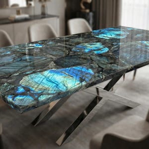 Puede incluir: Una mesa de comedor rectangular con una encimera de labradorita pulida. La piedra presenta llamativos patrones azules y turquesas sobre un fondo oscuro. La mesa está sostenida por una base de acero inoxidable pulido.