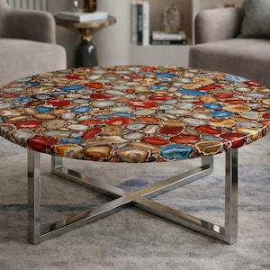 May include: A circular coffee table featuring a mosaic top made from polished agate stones in red, blue, brown, and cream hues. The table has a polished chrome base with crossed legs.