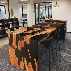 May include: A bespoke wooden bar with a black epoxy resin surface. The bar showcases a natural wood grain design with a dark finish. It is complemented by black bar stools, offering a contemporary aesthetic. Suitable for home or commercial use, the bar is a statement piece.