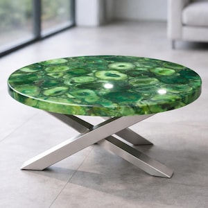 May include: Round coffee table with a vibrant green agate stone top. The tabletop features a unique pattern of green and white swirls. The table has a modern design with a brushed metal X-shaped base.