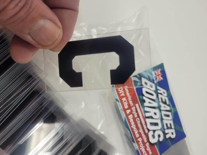 Puede incluir: Una letra "C" negra, de forma octogonal, sobre una l&aacute;mina de pl&aacute;stico transparente, sostenida por una mano. La imagen tambi&eacute;n muestra una pila de l&aacute;minas similares y un letrero de Reader Boards con el texto: "American Style Changeable Signs DIY Kits & Bespoke Projects."