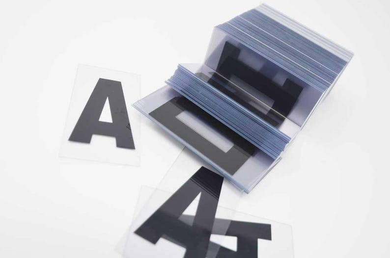 Puede incluir: Una pila de l&aacute;minas de pl&aacute;stico transparente con la letra "A" negra impresa. Varias letras "A" individuales est&aacute;n dispersas. Las letras est&aacute;n en una fuente negrita sin serifa.