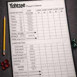 May include: A Yahtzee game set, including a score sheet, dice, and a pencil. The white score sheet has black text and grid lines. Six dice are scattered on the surface, along with red game pieces and two green dice.