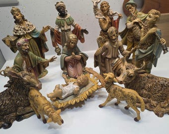 Può includere: Un set per presepe con statuine in resina dipinte a mano che include il bambino nella mangiatoia, Maria, Giuseppe, i tre re magi, pastori e vari animali come un asino, pecore e un bue, tutti realizzati in tonalità terra tenui.